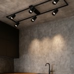 Lampa sufitowa Bumo w kolorze czarnym, z sześcioma punktami świetlnymi GU10, zamontowana na prostokątnej ramie. Widok z dołu, w nowoczesnym wnętrzu z betonowymi ścianami i drewnianym blatem.
