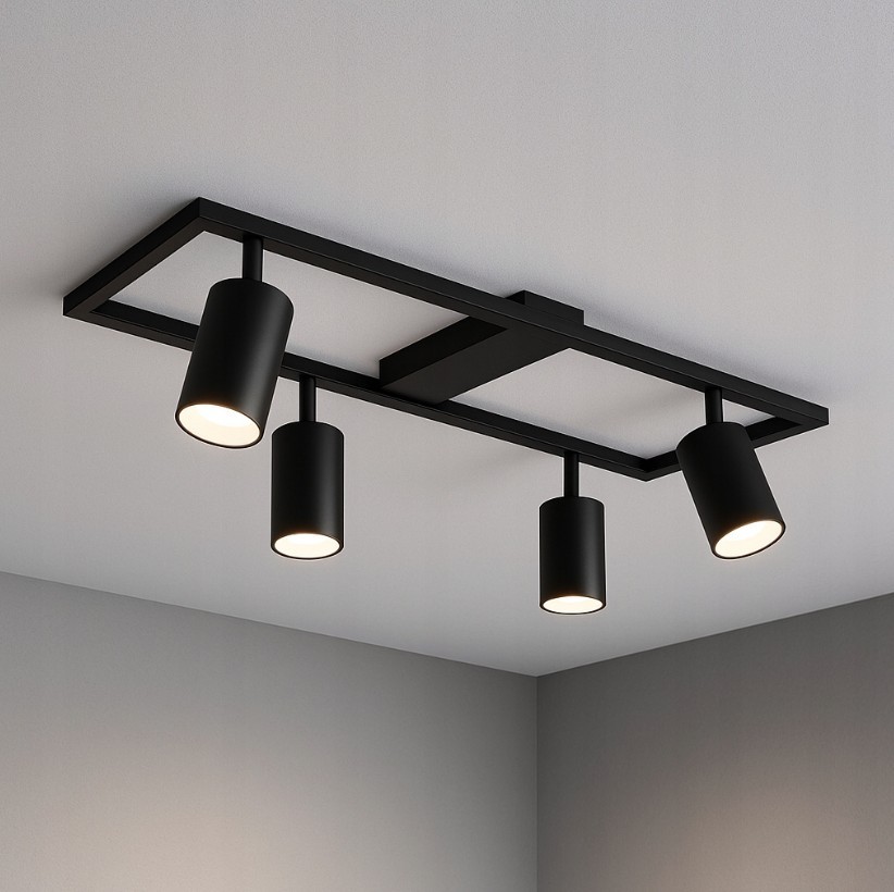 Czarna lampa sufitowa Bumo z czterema reflektorami GU10, zamontowana na prostokątnej podstawie. Reflektory w formie cylindrów, skierowane w różnych kierunkach. Lampa wisząca, umieszczona na jasnym tle.