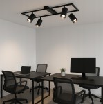 Czarna lampa sufitowa Bumo z czterema reflektorami GU10, zamontowana na prostokątnej podstawie. Reflektory są skierowane w różne strony, o cylindrycznym kształcie. Lampa znajduje się w nowoczesnym biurze z czarnymi biurkami i krzesłami.