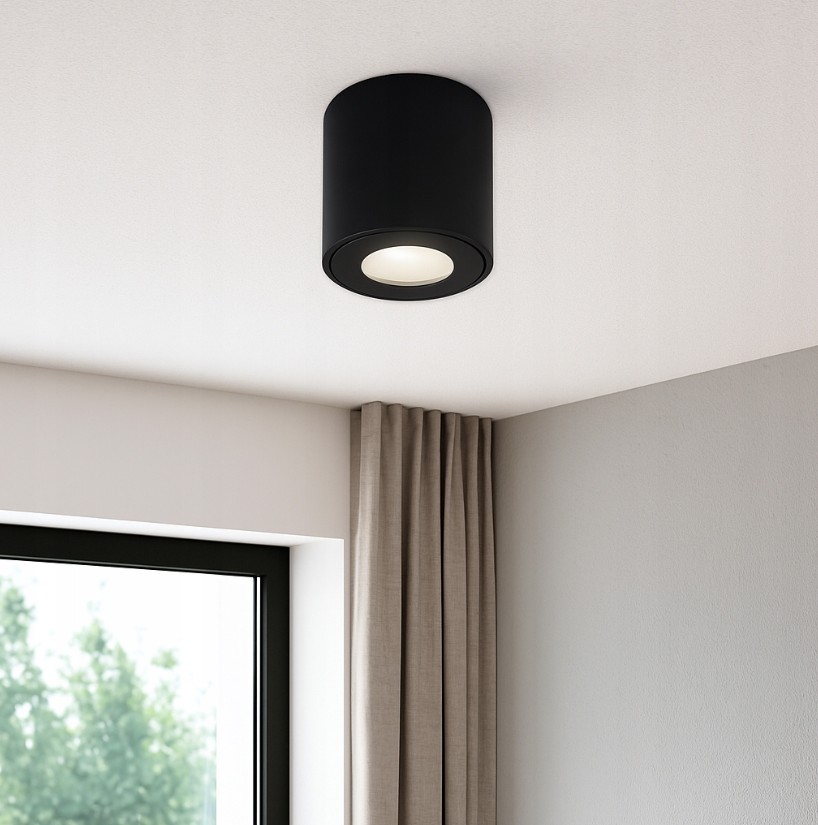 Czarna lampa sufitowa tuba Aqua IP54, zamontowana na suficie, z okrągłym źródłem światła. Widoczny jest gładki, matowy materiał oraz minimalistyczny design. Tło to jasna ściana i zasłony w odcieniu beżowym.