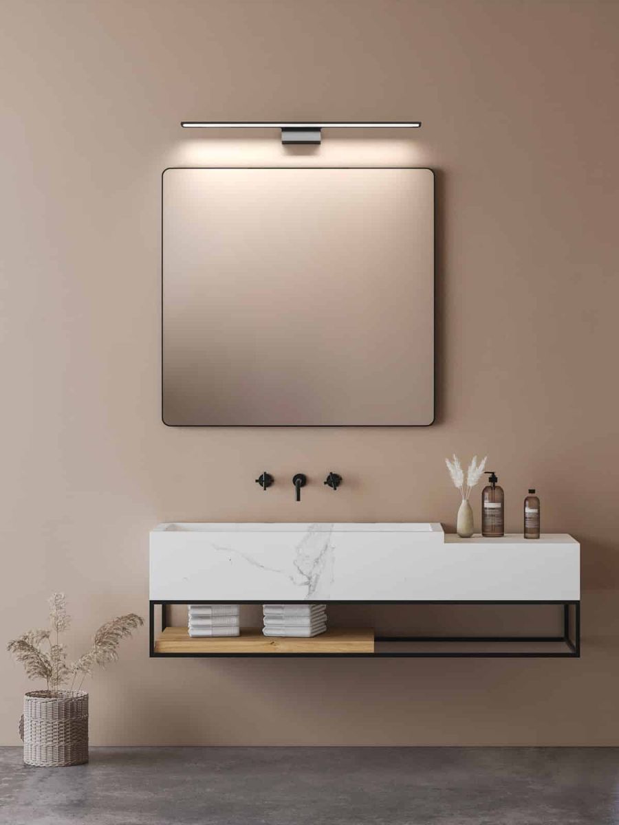 Luce Parette Nero 62 IP44 kinkiet LED 11W CCT w kolorze czarnym, zamontowany nad lustrem w łazience. Prosty, minimalistyczny design z metalowym mocowaniem, emitujący ciepłe światło, w otoczeniu nowoczesnej umywalki i dekoracji.