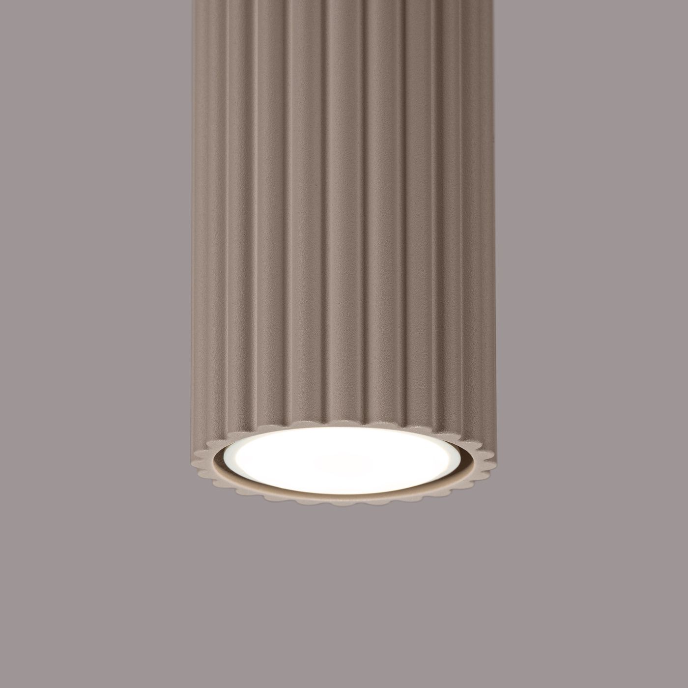 Lampa sufitowa Karbon 10 l w kolorze taupe z fakturowaną obudową w pionowe prążki. Okrągła oprawa na jedną żarówkę GU10, z widocznym białym kloszem. Produkt zamontowany, widok z dołu. Tło w jednolitym, szarym odcieniu.