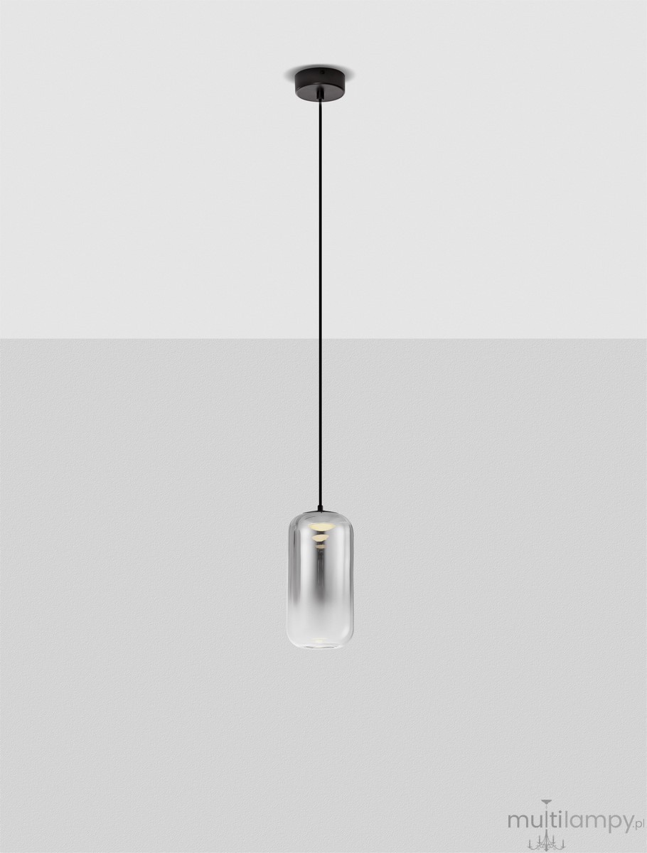 Czarna lampa wisząca Anuco z jedną żarówką LED 3W, z cylindrycznym, transparentnym kloszem. Wisi na cienkim, czarnym kablu, montowana do sufitu. Tło jasnoszare, podkreślające minimalistyczny design.