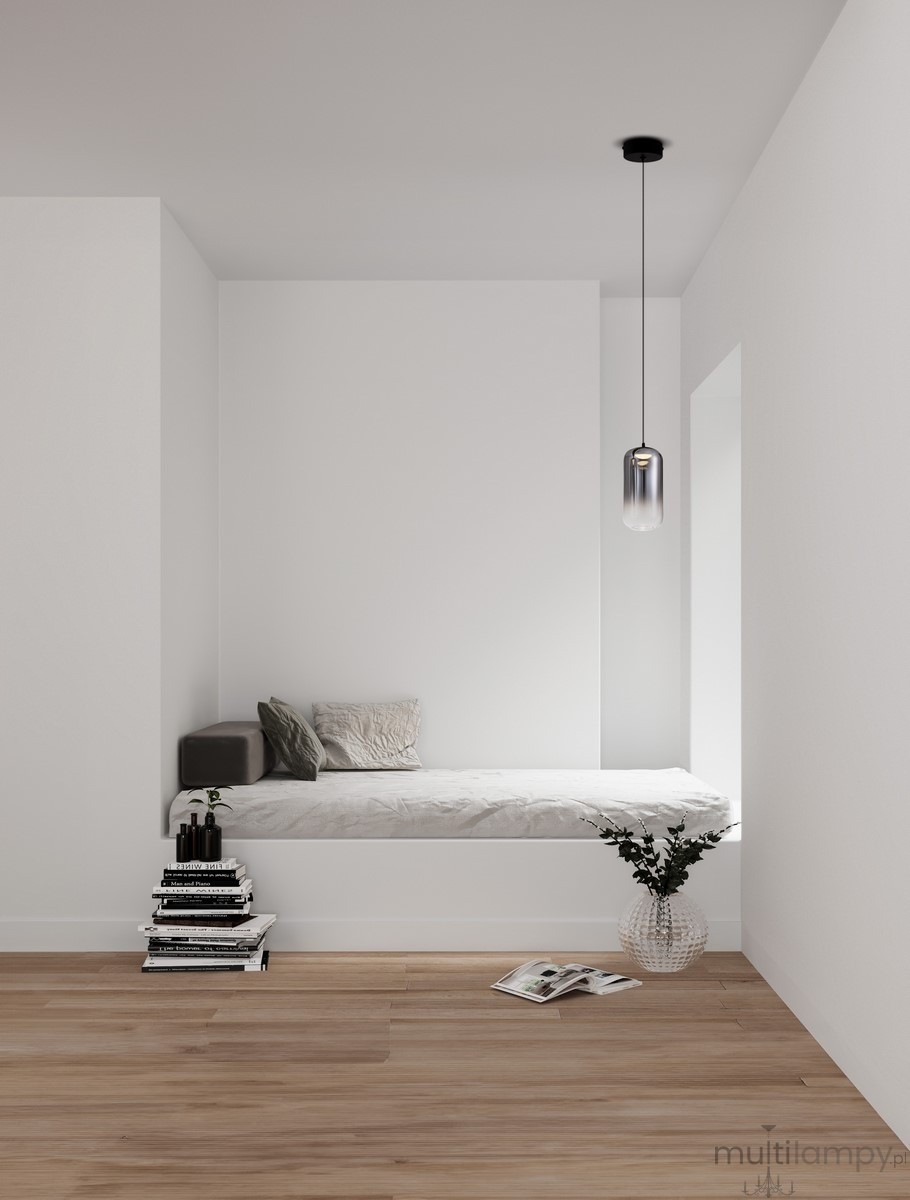 Czarna lampa wisząca Anuco z jedną diodą LED 3W, o cylindrycznym kształcie, zawieszona na cienkim przewodzie. Lampa znajduje się w minimalistycznym wnętrzu z łóżkiem, książkami i rośliną w wazonie. Tło jest jasne, co podkreśla jej nowoczesny design.