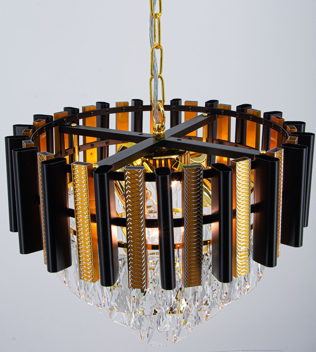 Lampa wisząca Bilbao 4xE27 w kolorze złotym i czarnym, o okrągłej konstrukcji z elementami szklanymi. Widoczne czarne, metalowe rurki oraz kryształowe detale u dołu. Zawieszona na łańcuszku, z eleganckim wykończeniem.