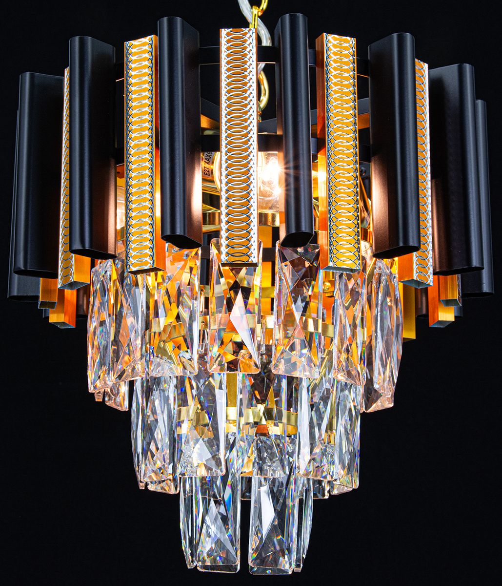 Lampa wisząca Bilbao z trzema oprawami E14. Czarne, cylindryczne elementy z metalicznymi wstawkami i kryształowymi zwisami. Kąt ujęcia zbliżony na detal, wisząca konstrukcja. Elegancki design z połyskującymi akcentami złota.
