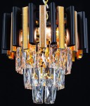 Lampa wisząca Bilbao z trzema oprawami E14. Czarne, cylindryczne elementy z metalicznymi wstawkami i kryształowymi zwisami. Kąt ujęcia zbliżony na detal, wisząca konstrukcja. Elegancki design z połyskującymi akcentami złota.