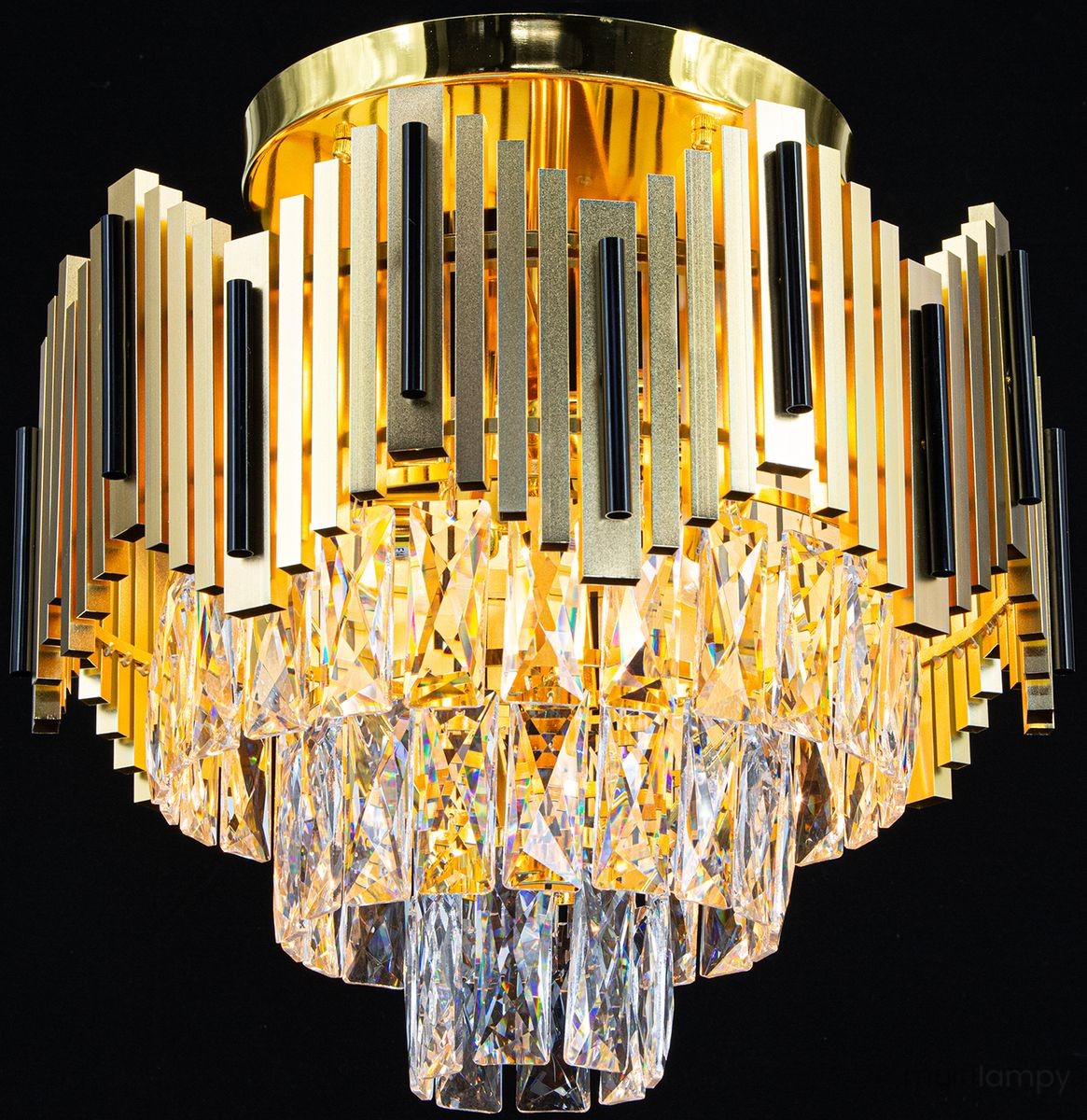 Lampa sufitowa Belize 4xE27 w kolorze złotym i czarnym. Konstrukcja z metalowych, prostokątnych elementów oraz kryształowe wiszące detale tworzą elegancki efekt. Widok z góry, lampa zamontowana na suficie, emitująca ciepłe światło.