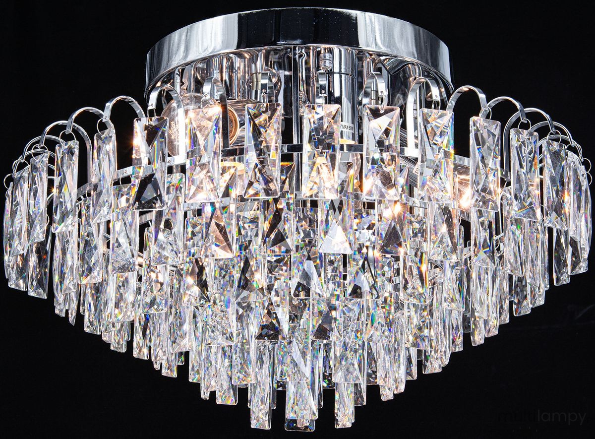 Lampa sufitowa Monaco w chromowanej obudowie, z sześcioma miejscami na żarówki E27. Posiada kryształowe elementy w formie wiszących, prostokątnych dekoracji, które odbijają światło, tworząc efektowną iluminację. Ujęcie z dołu, na jednolitym tle.