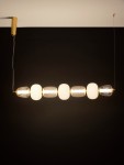 Lampa wisząca Arroyos 1xLED 42W w kolorze złotym, z sześcioma okrągłymi i cylindrycznymi kloszami, z przezroczystego i matowego szkła. Zawieszona na cienkim drucie, z montażem sufitowym, na jednolitym, ciemnym tle.
