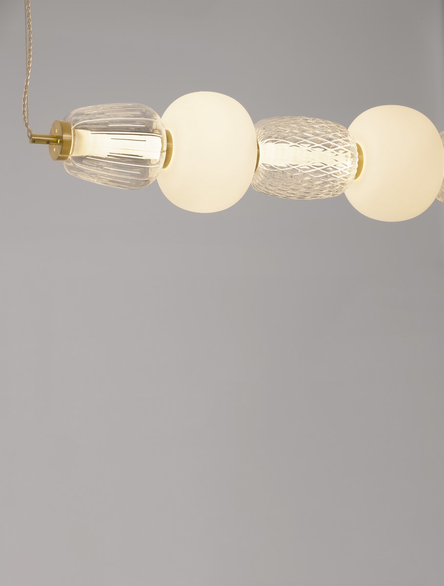 Lampa wisząca Arroyos z jednym źródłem LED o mocy 42W, złożona z trzech kulistych elementów: dwóch szklanych o fakturze oraz jednego matowego, w kolorze złotym, zawieszona na cienkim przewodzie. Tło szare.