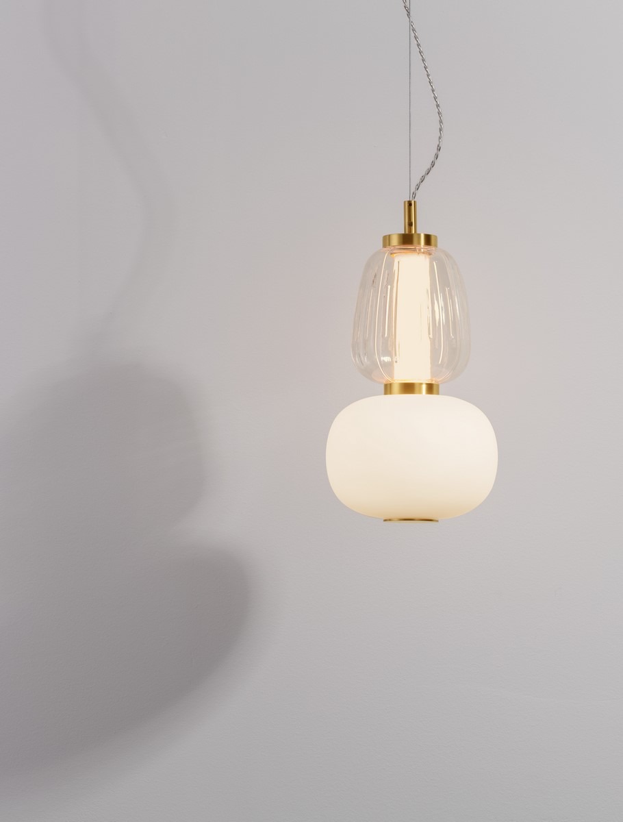 Lampa wisząca Arroyos z jednym źródłem LED 18W, złota. Składa się z dwóch elementów: górnej, przezroczystej klosza o żłobieniach i dolnej, matowej, okrągłej części. Ujęcie frontalne, zawieszona na cienkim przewodzie na jasnym tle.