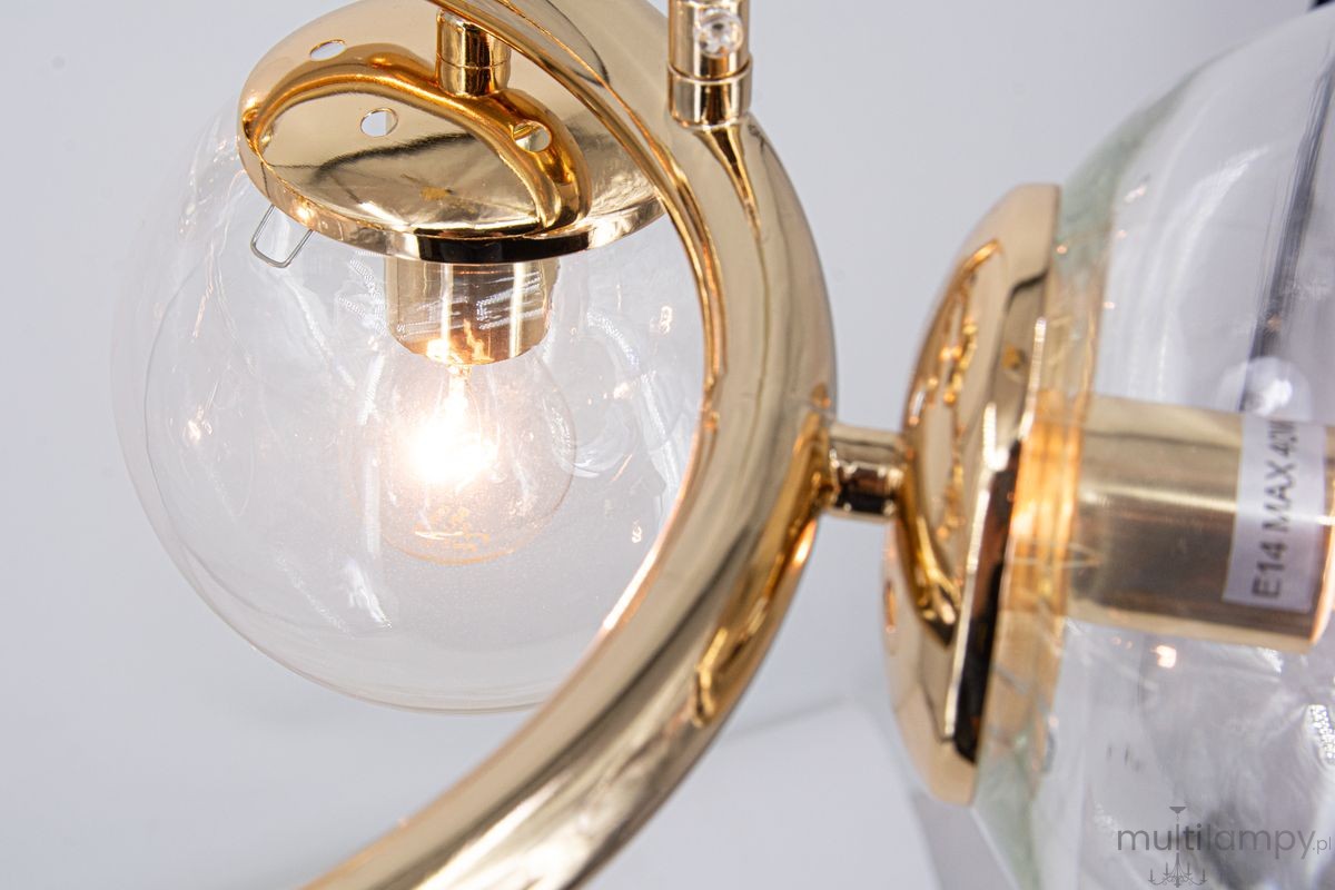 Lampa wisząca Amaro w kolorze złotym, z pięcioma oprawami E14. Ujęcie zbliżeniowe na jedną z kulistych szklanych kloszy, w której widoczna jest żarówka. Elementy metalowe mają błyszczącą fakturę, a klosz jest transparentny.