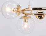 Lampa wisząca Amaro 5xE14 w kolorze złotym. Posiada pięć przezroczystych kloszy w kształcie kul, zawieszonych na złotej metalowej konstrukcji. Ujęcie z bliska, ukazujące detale wykończenia i źródeł światła. Tło białe.