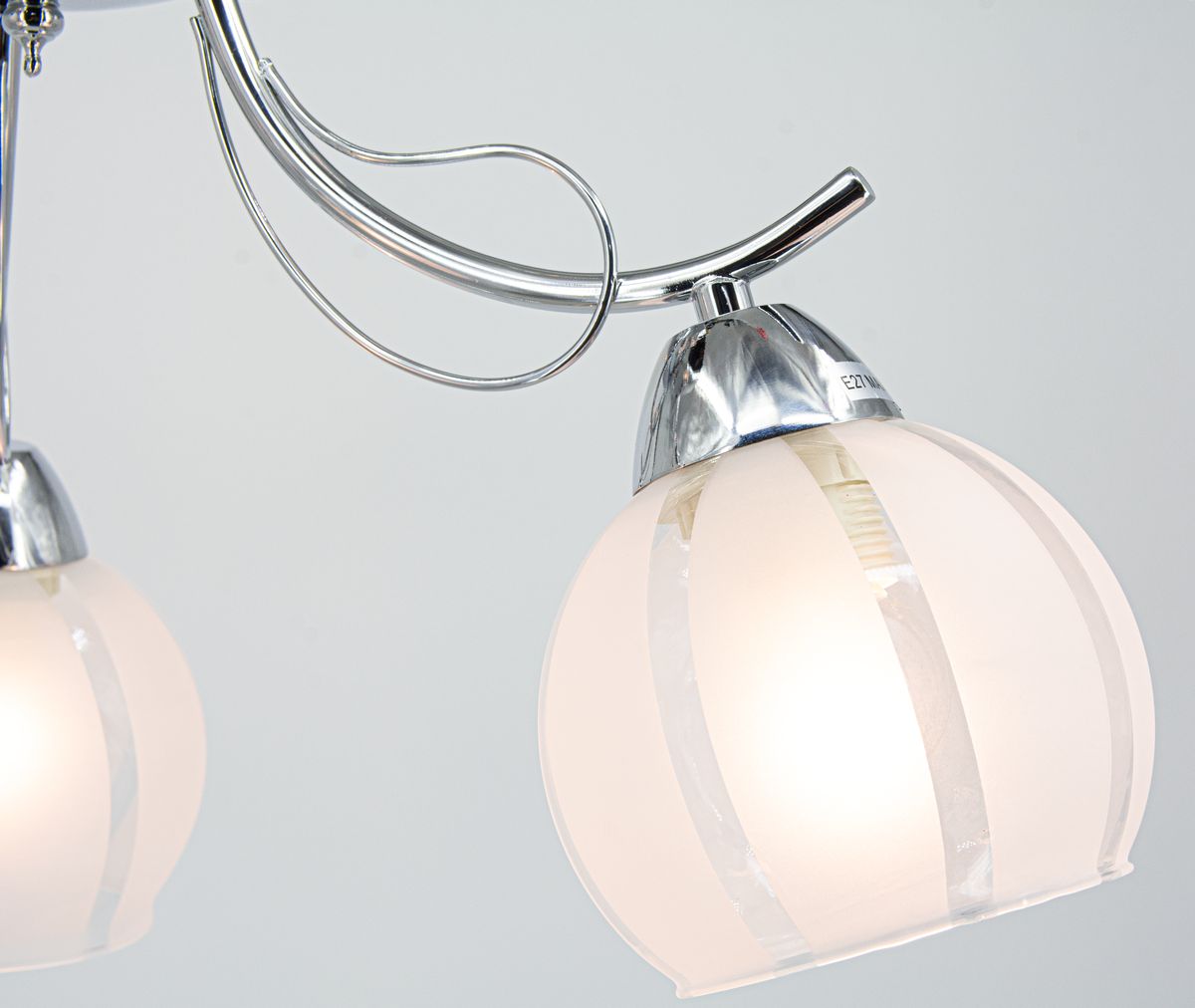 Lampa sufitowa Faro z trzema kloszami E27 w chromowanym wykończeniu. Klosze w kształcie kulistym, wykonane z matowego szkła z przezroczystymi pasami. Ujęcie z boku, ukazujące detale konstrukcji oraz stylowy design.