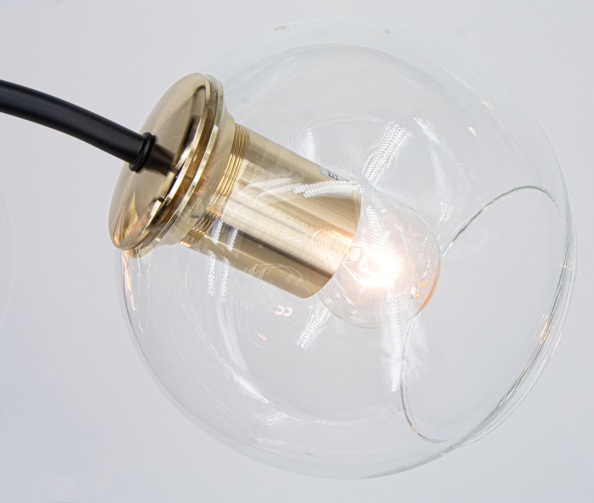 Lampa sufitowa Elba 4xE27 w kolorze czarnym i złotym z przezroczystym kloszem. Widok z góry na detal oprawy, metalowy element w złotym wykończeniu z żarówką wewnątrz, zawieszona na czarnym przewodzie.