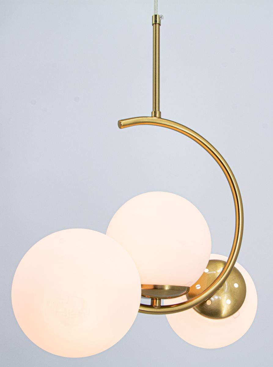 Lampa wisząca Luna z mosiądzu, z trzema okrągłymi kloszami w białym kolorze. Ujęcie z przodu, z cienką metalową rurką podtrzymującą. Klasyczny design, idealna do nowoczesnych wnętrz. Wymiary kloszy są jednorodne, a powierzchnia jest gładka.