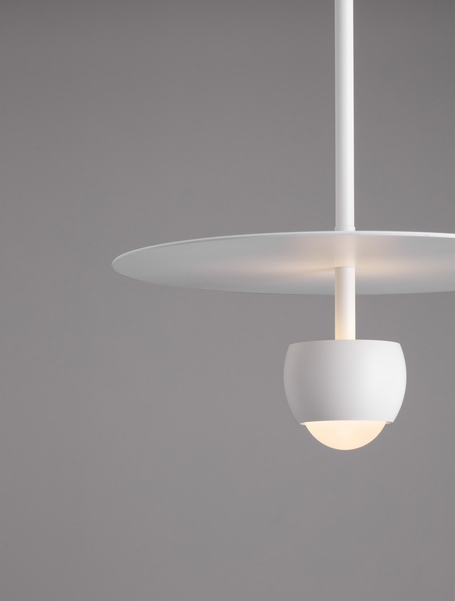 Lampa wisząca Baila w kolorze białym, z jedną żarówką LED 8W. Okrągła, płaska podsufitka z metalu, z oprawą w kształcie półkuli. Prosty design, zawieszona na cienkim przewodzie, na jednolitym tle.