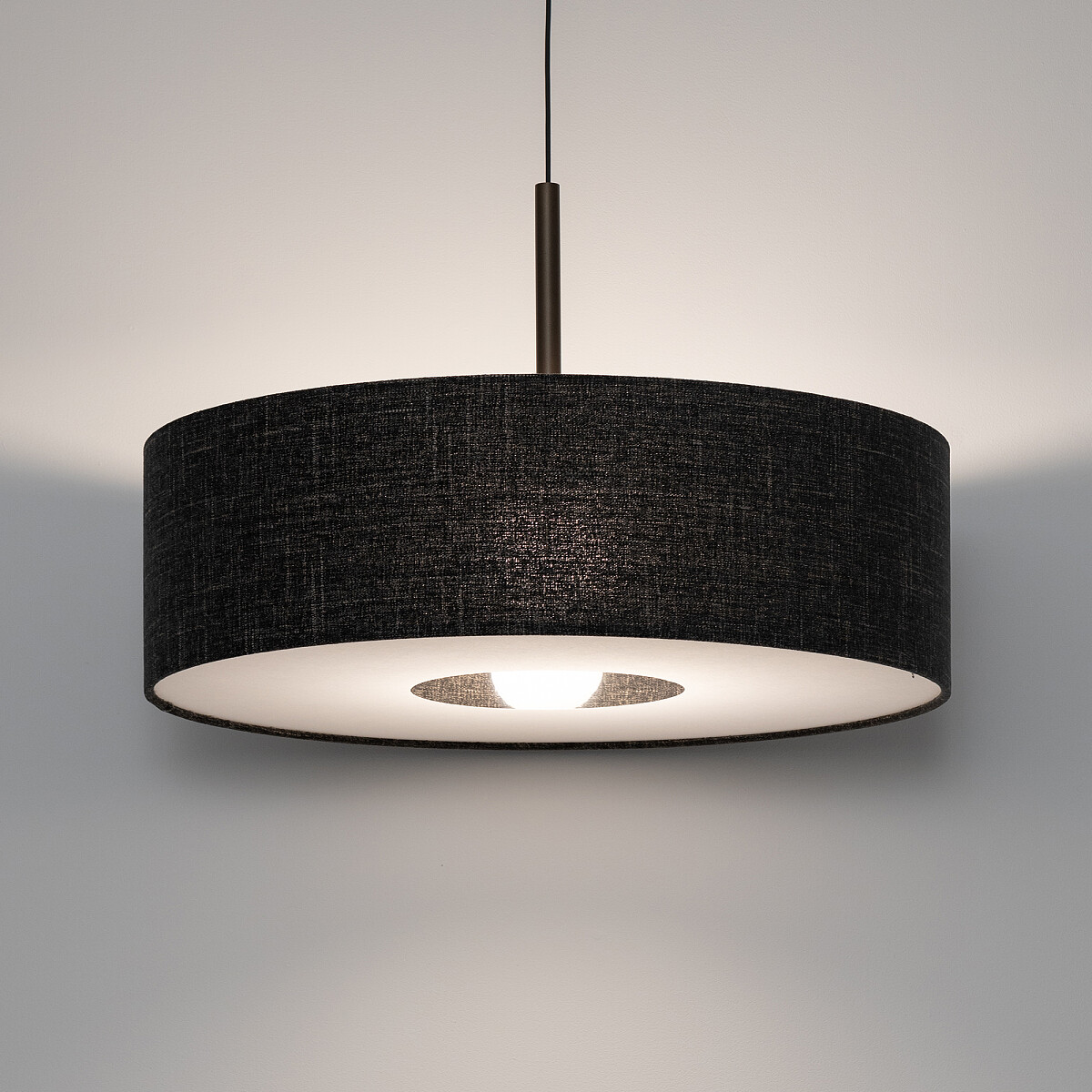 Lampa wisząca Amarela L w kolorze czarnym melanż, z okrągłym kloszem z tkaniny, zawieszona na cienkim przewodzie. Wewnętrzna część klosza w jasnym kolorze, z widocznym miejscem na żarówkę E27. Zawieszona w pozycji centralnej, na jednolitym tle.
