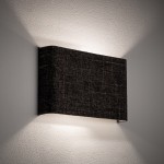 Kinkiet Amarela B w kolorze czarnym melanż, o prostokątnej formie, zamontowany na ścianie. Emituje ciepłe światło, tworząc delikatne refleksy na powierzchni. Widoczna tekstura materiału na obudowie.