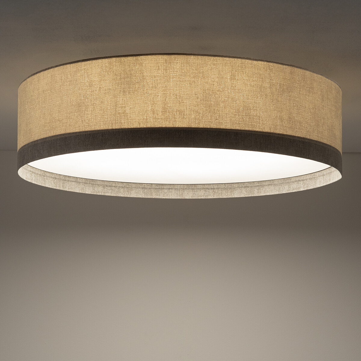 Lampa sufitowa Cedro L w kolorze beżowym, o okrągłym kształcie. Wykonana z materiału o teksturowanej powierzchni, z białym kloszem wewnętrznym. Zawiera miejsce na żarówkę E27, montowana na suficie, widok z dołu.