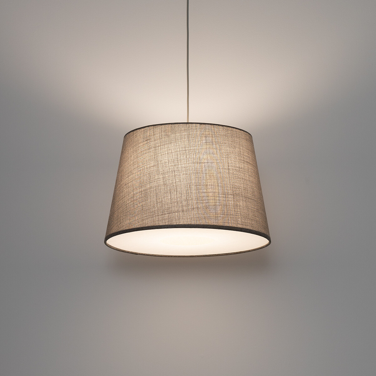 Lampa wisząca Tutoia z abażurem w odcieniu beżowym, wyposażona w jedno gniazdo E27. Ujęcie frontalne, lampa zawieszona na cienkim przewodzie, emitująca miękkie światło. Abażur z teksturowanej tkaniny, lekko zaokrąglony u góry i na dole.