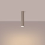 Lampa sufitowa Karbon 30 w kolorze taupe, cylindryczna, z teksturowaną powierzchnią i jednym gniazdem GU10. Zawieszona w pionie, emituje światło, podkreślając subtelne odcienie ściany. Tło w jednolitym, jasnym kolorze.