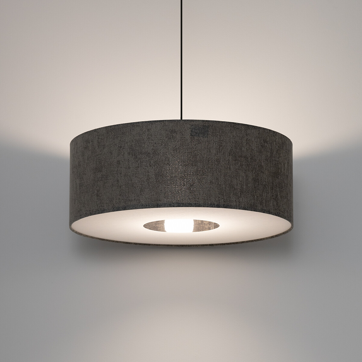 Lampa wisząca Lago M w kolorze szarym, z okrągłym abażurem z tkaniny. Ujęcie frontalne, wisi na cienkim przewodzie. Wewnątrz widoczna oprawka na żarówkę E27, emitująca miękkie światło, z subtelnym cieniem na ścianie.