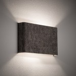 Kinkiet Lago B w kolorze szarym, z jedną oprawką G9, o prostokątnym kształcie. Ujęcie z boku, montowany na ścianie, emitujący światło w górę i w dół, z teksturowaną powierzchnią. Tło proste, co podkreśla elegancki design lampy.
