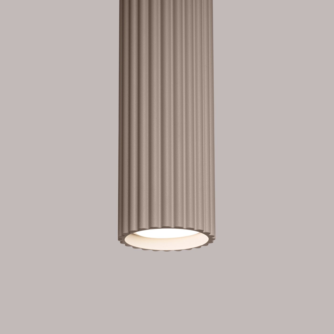 Lampa wisząca Karbon w kolorze taupe, z cylindrycznym kloszem o żłobionej fakturze, przeznaczona na żarówkę typu GU10. Ujęcie z bliska, pokazujące detale klosza i jego dolną część z białym wykończeniem. Tło w delikatnym odcieniu szarości.