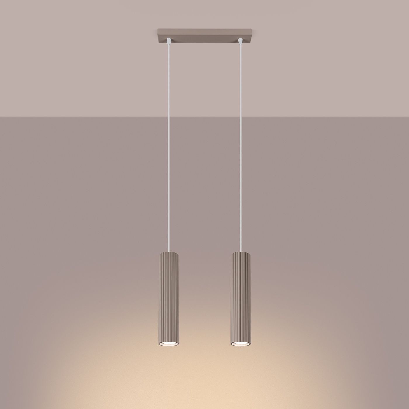 Lampa wisząca Karbon 2 w kolorze taupe z dwoma cylindrycznymi kloszami z pionowymi żłobieniami. Zawieszona na białych linkach, przymocowana do prostokątnej podsufitki. Oświetlenie z dwoma gniazdami GU10.