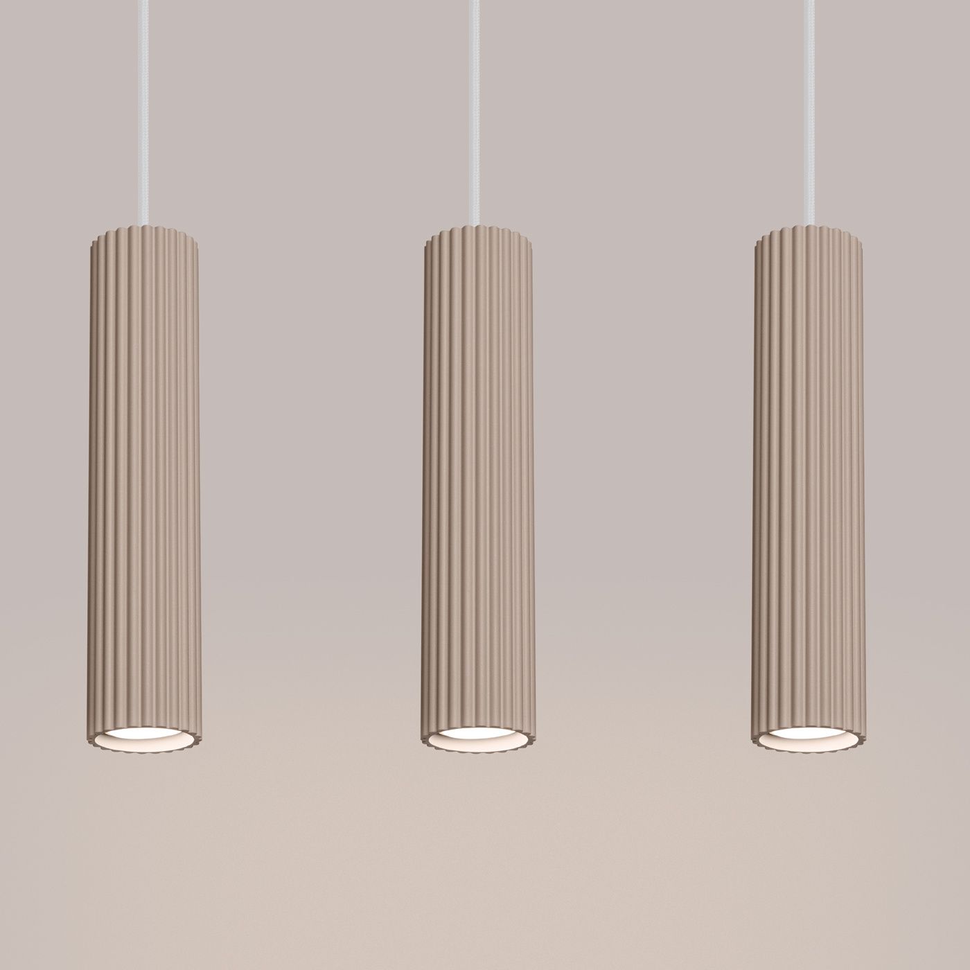 Lampa wisząca Karbon 3 o kolorze taupe z trzema cylindrycznymi kloszami w pionie, wykonana z teksturowanego materiału. Montowana na białych przewodach, każdy klosz zawiera miejsce na żarówkę GU10. Tło w jasnym odcieniu.