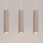 Lampa wisząca Karbon 3 o kolorze taupe z trzema cylindrycznymi kloszami w pionie, wykonana z teksturowanego materiału. Montowana na białych przewodach, każdy klosz zawiera miejsce na żarówkę GU10. Tło w jasnym odcieniu.