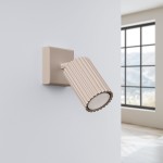 Kinkiet Karbon 1xGU10 w kolorze taupe, z cylindrycznym kloszem o żłobionej fakturze, zamontowany na prostokątnej podstawie. Ujęcie z boku, w tle jasne wnętrze z dużym oknem.