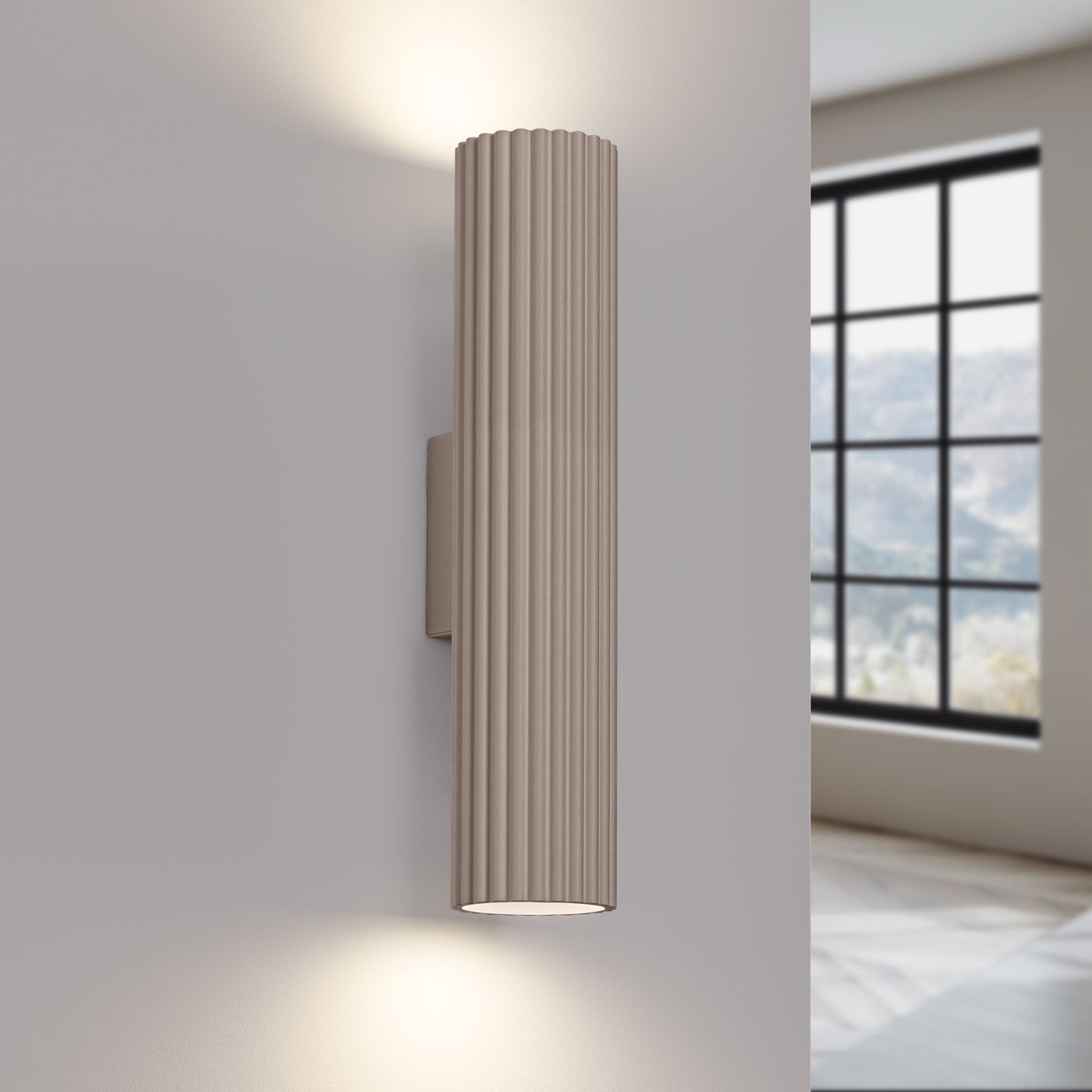 Kinkiet Karbon 30 w kolorze taupe, z dwoma oprawami GU10, o cylindrycznym kształcie i żłobionej fakturze. Ujęcie frontalne, zamontowany na ścianie, emitujący światło w górę i w dół, w jasnym wnętrzu z dużym oknem w tle.