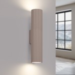 Kinkiet Karbon 30 w kolorze taupe, z dwoma oprawami GU10, o cylindrycznym kształcie i żłobionej fakturze. Ujęcie frontalne, zamontowany na ścianie, emitujący światło w górę i w dół, w jasnym wnętrzu z dużym oknem w tle.