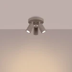 Lampa sufitowa Karbon w kolorze taupe, z trzema regulowanymi reflektorami GU10. Ułożona płasko na suficie, z okrągłą podstawą i żeberkowanymi kloszami, emitującym ciepłe światło. Tło w jasnym odcieniu, podkreślające design lampy.