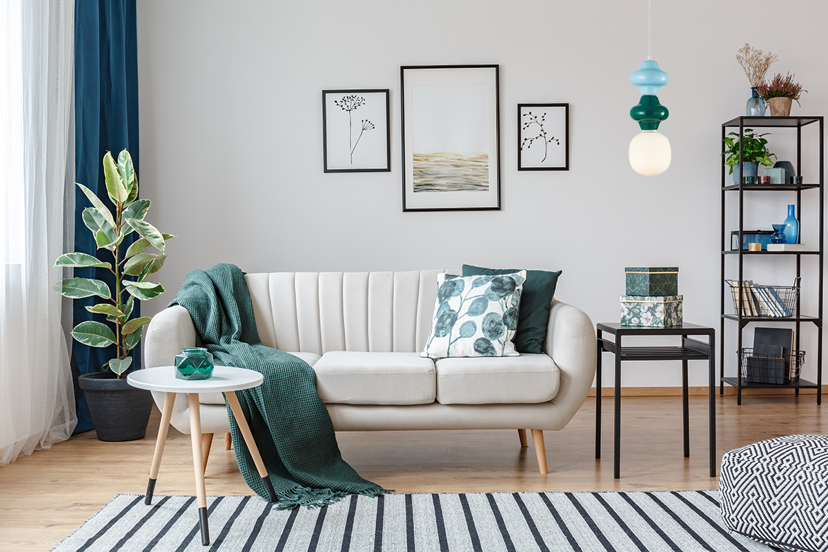Lampa wisząca Latera 1xE14 w multikolorze, złożona z okrągłej białej części oraz kilku kolorowych elementów w odcieniach zieleni i błękitu. Zawieszona nad sofą w jasnym wnętrzu, dodaje kolorowego akcentu do aranżacji.