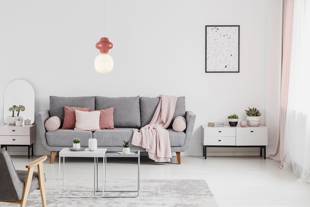Lampa wisząca Latera 1xE14 w multikolorze, z okrągłym, mlecznym kloszem i czerwono-różowym zdobieniem, zawieszona nad szaro-różową sofą w nowoczesnym wnętrzu, na jasnym tle z dodatkami roślinnymi.
