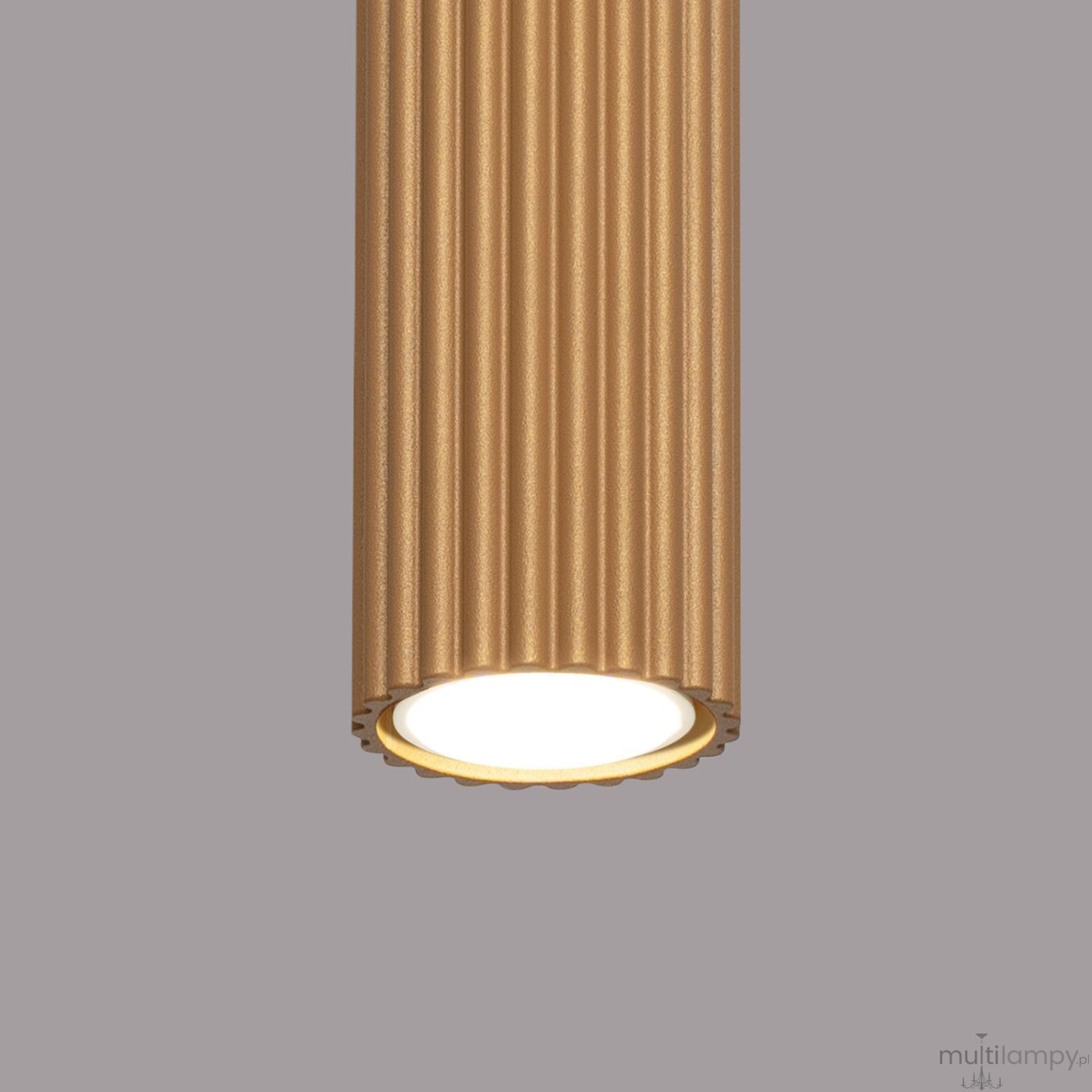 Lampa sufitowa Karbon 60 w kolorze złotym, o cylindrycznym kształcie z falistą teksturą. Posiada oprawę na jedną żarówkę GU10. Ujęcie z dołu, pokazujące szczegóły dekoracyjne oraz źródło światła. Tło w odcieniu szaro-beżowym.