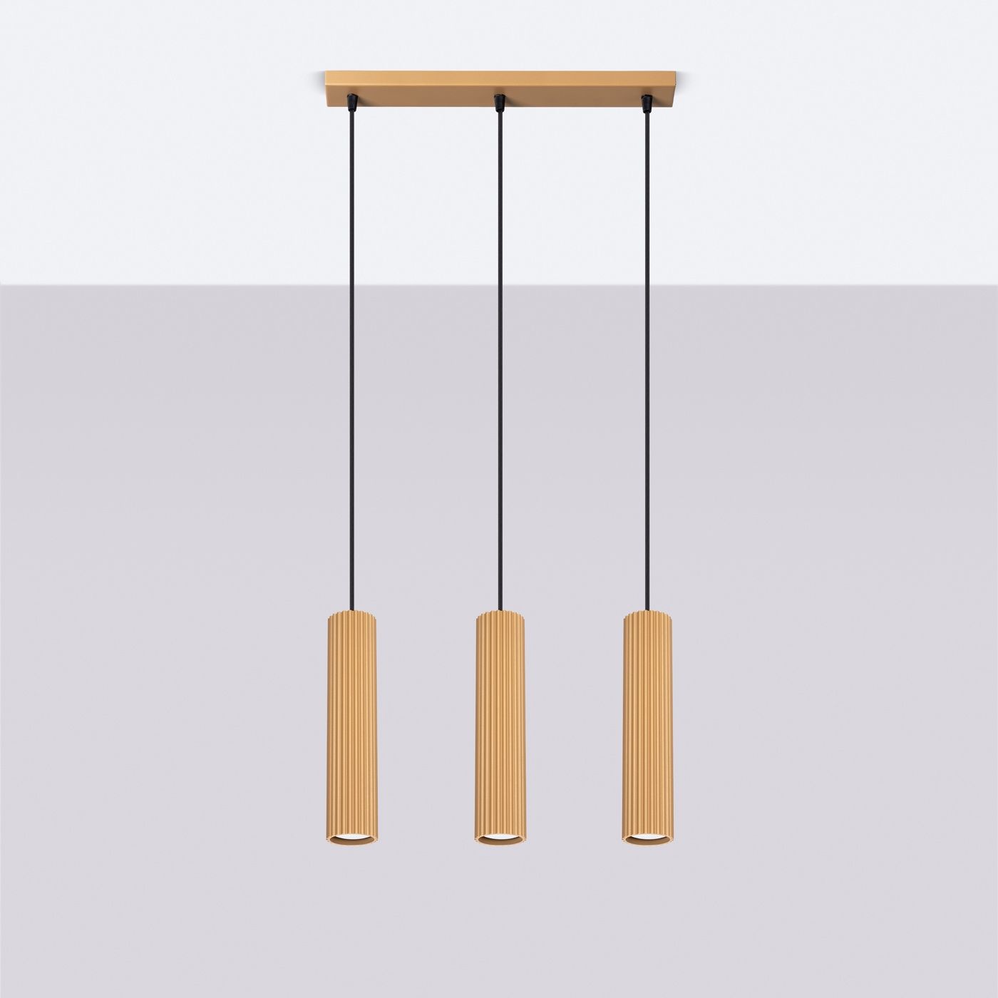 Lampa wisząca Karbon 3, złota, z trzema cylindrycznymi kloszami o żebrowanej fakturze, zawieszona na czarnych linkach. Ujęcie frontalne, na tle jasnej ściany, podkreślające nowoczesny design i elegancki styl.