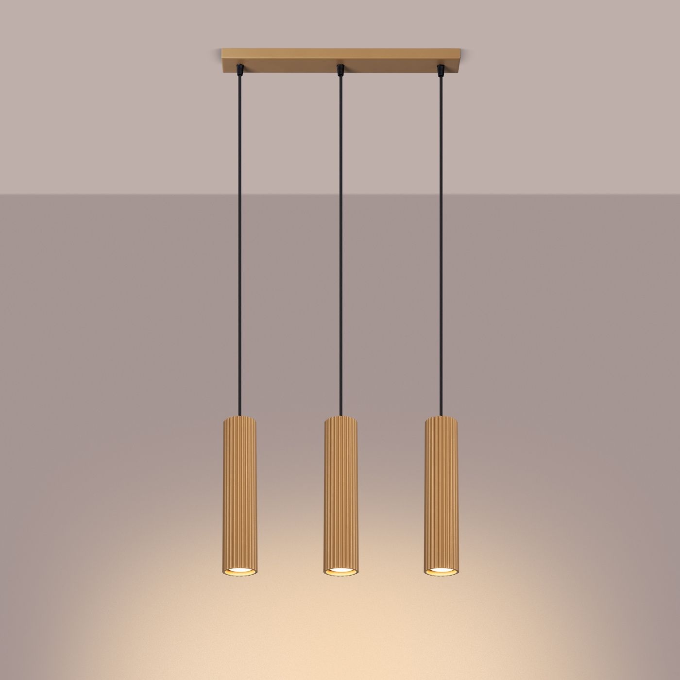 Lampa wisząca Karbon 3, złota, z trzema cylindrycznymi kloszami z rowkowaną fakturą, zawieszona na czarnych linkach. Ujęcie frontalne, oświetlenie skierowane w dół, na jednolitym tle.