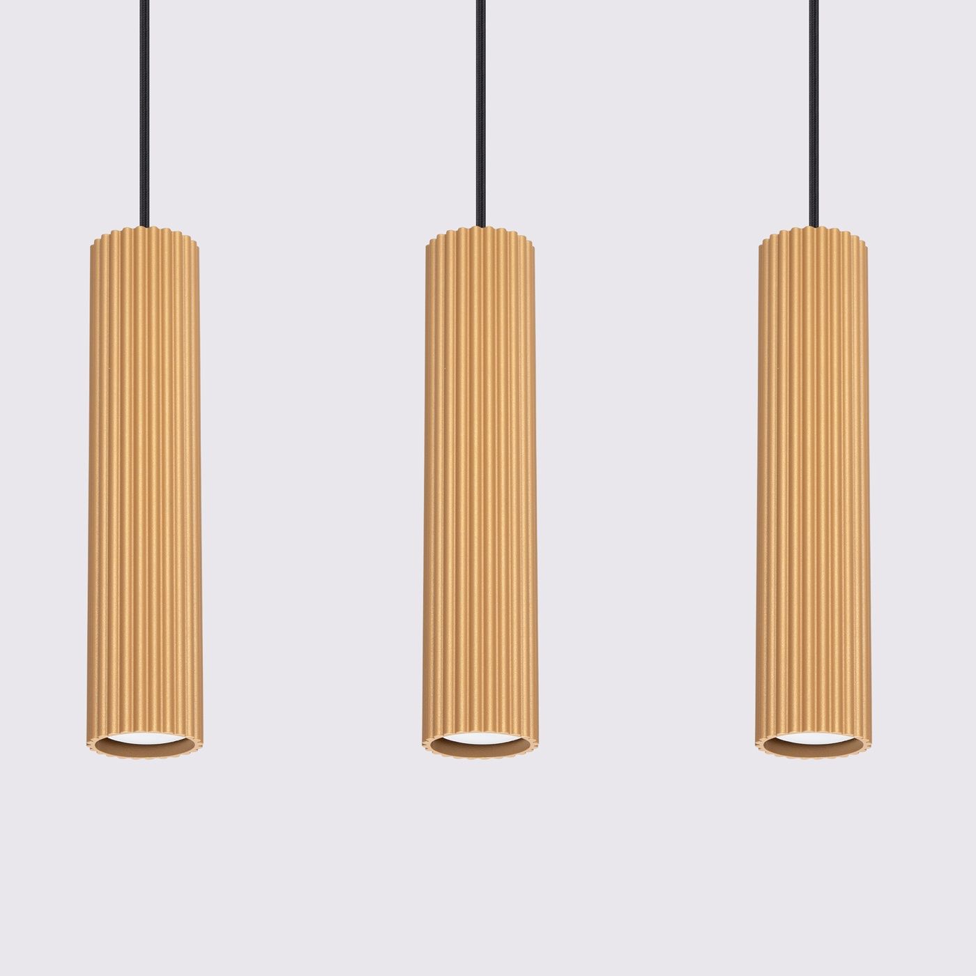 Lampa wisząca Karbon 3 z trzema złotymi, cylindrycznymi kloszami o fakturze żłobkowanej, zawieszona na czarnych przewodach. Klosze są umieszczone równolegle, tworząc nowoczesny design. Tło jasnoszare, co podkreśla kolor lampy.
