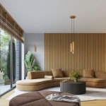 Lampa wisząca Karbon 3P w złotym kolorze z trzema miejscami na żarówki GU10, zawieszona na długich linkach, umieszczona w nowoczesnym wnętrzu z brązową sofą i okrągłym stołem. Tło stanowi drewniana ściana i duże okno z widokiem na roślinność.