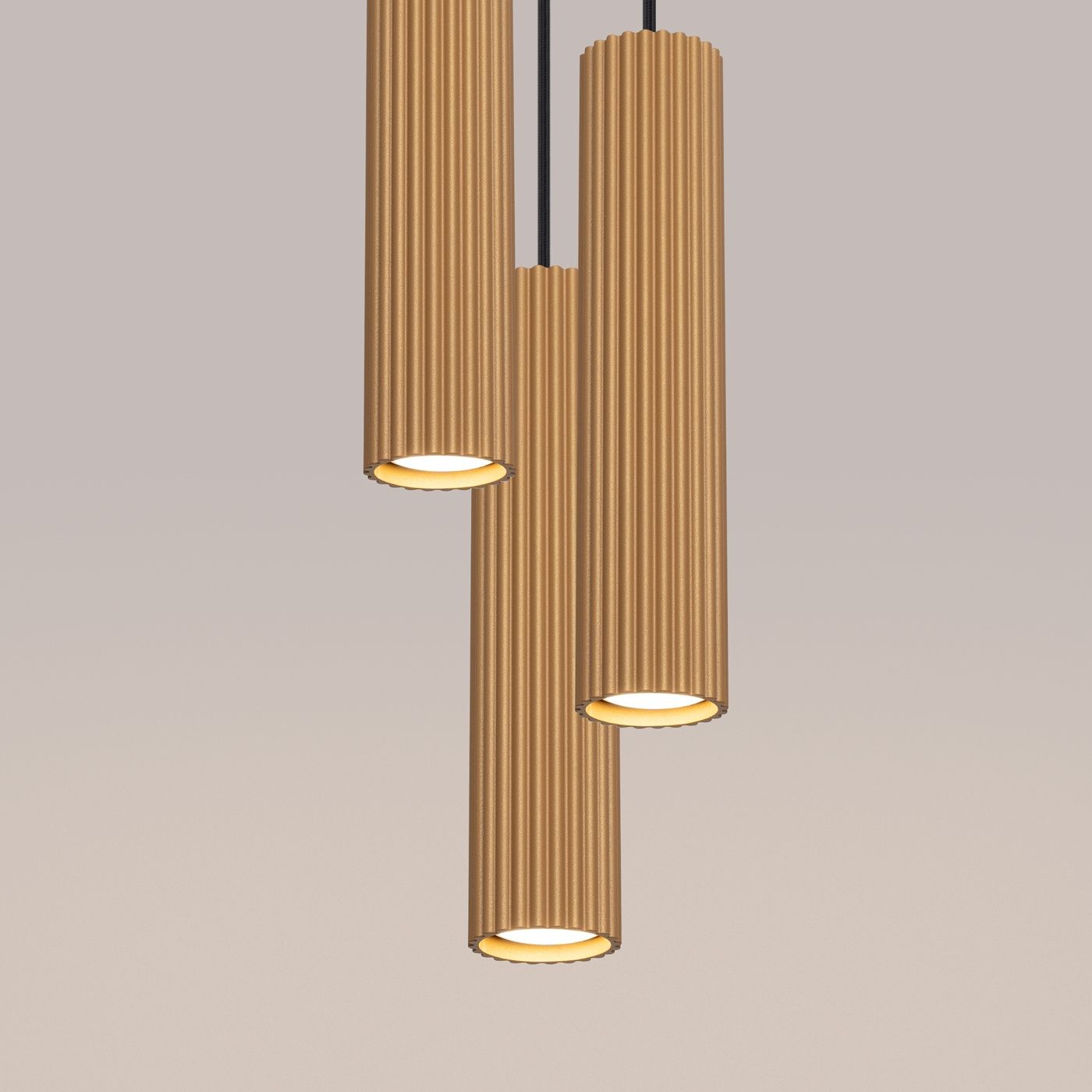 Lampa wisząca Karbon 3P w kolorze złotym, składająca się z trzech cylindrycznych kloszy z żłobieniami. Ujęcie z góry, z widocznymi oprawkami GU10. Lampa zawieszona na czarnych przewodach, na jednolitym tle. Idealna do nowoczesnych wnętrz.