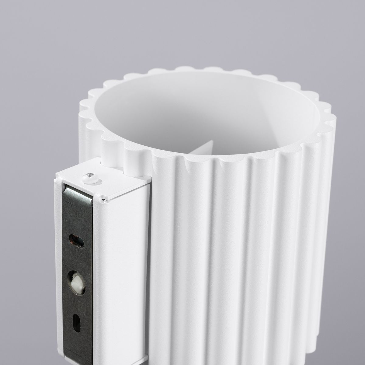 Kinkiet Aura 1xG9 w kolorze białym, z fakturą ożebrowania na cylindrycznym korpusie. Widoczny metalowy element montażowy z otworami do mocowania. Produkt przedstawiony z bliska, ukazujący detale i kształt.