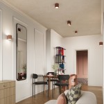 Kinkiet Aura 1xG9 w kolorze mocca, zamontowany na ścianie. Widoczne pionowe żłobienia na obudowie, emitujący ciepłe światło. W tle aranżacja wnętrza z lustrzanym odbiciem, stołem i krzesłami.