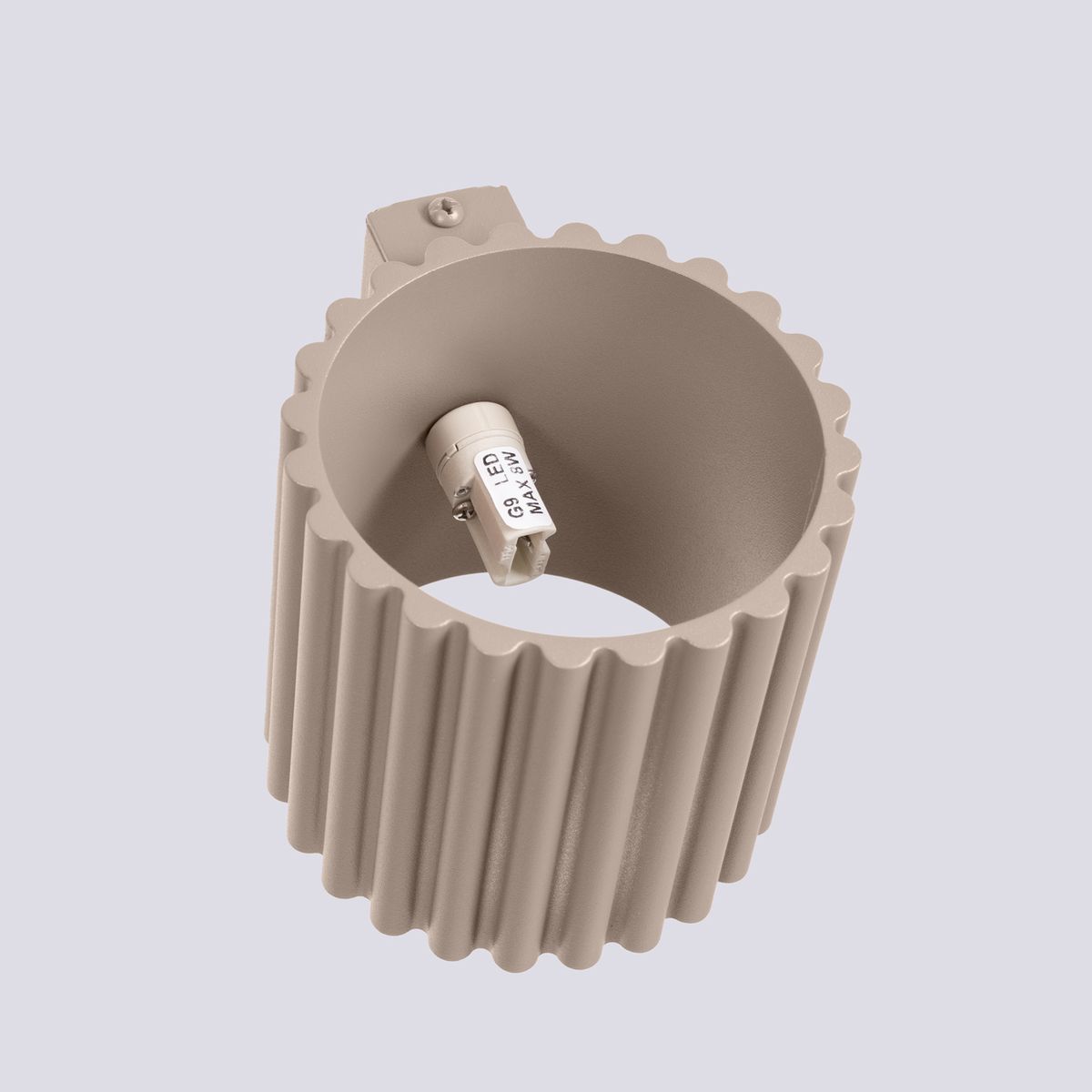 Kinkiet Aura w kolorze taupe, wykonany z materiału teksturowanego, z okrągłym kształtem i żłobieniami. Zainstalowane gniazdo na żarówkę G9 widoczne wewnątrz. Montażowy element na górze kinkietu, umieszczony na jasnym tle.