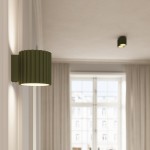 Kinkiet Aura 1xG9 w kolorze oliwkowej zieleni, z falistą fakturą klosza, zamontowany na ścianie. Światło kierowane jest w dół, w tle widoczne zasłony i okno.
