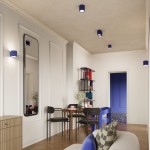 Lampa sufitowa Aura w kolorze ultramaryny z jedną oprawą GU10, zamontowana na suficie w nowoczesnym wnętrzu. W tle widoczna lustrzana ściana i drewniany stół z krzesłami. Oświetlenie podkreśla minimalistyczny styl aranżacji.